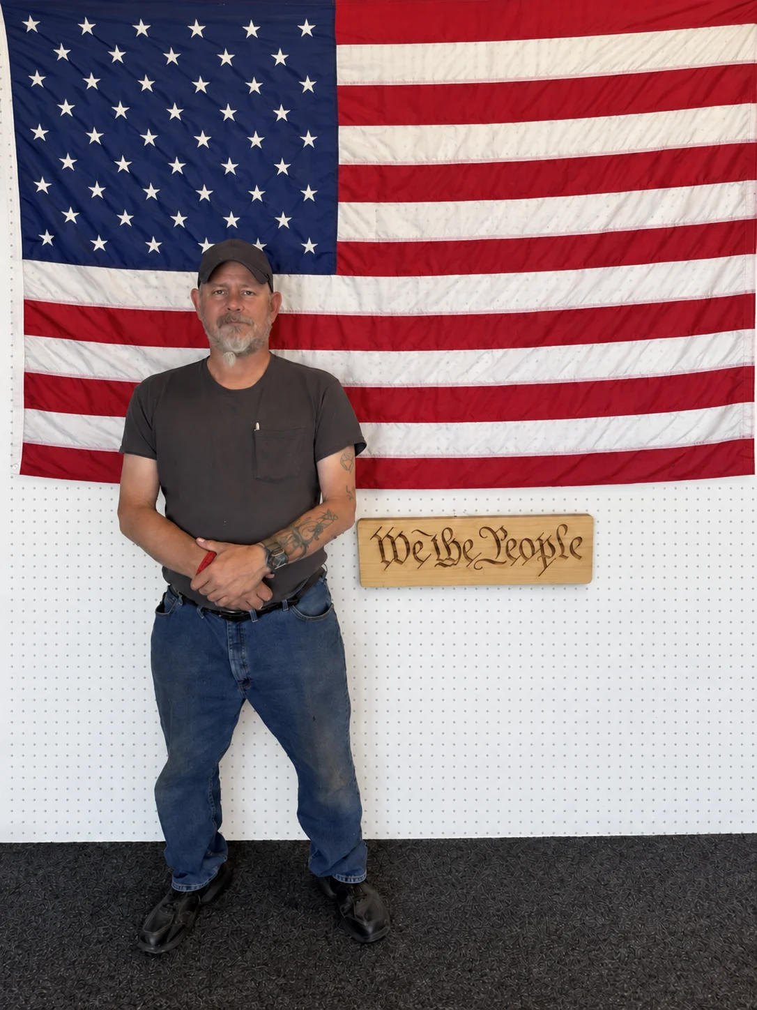 A team member standing in front of the shop's American flag and carved “We the People” sign
